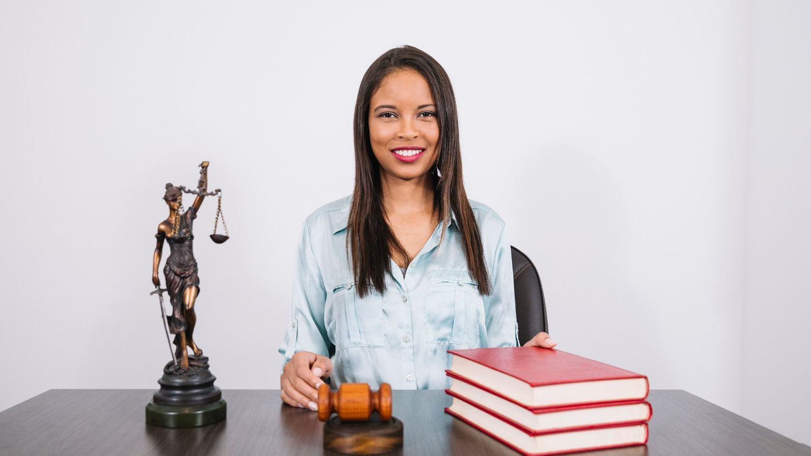 an image showing a cheerful African American woman on a table with gavel, books and statue. 